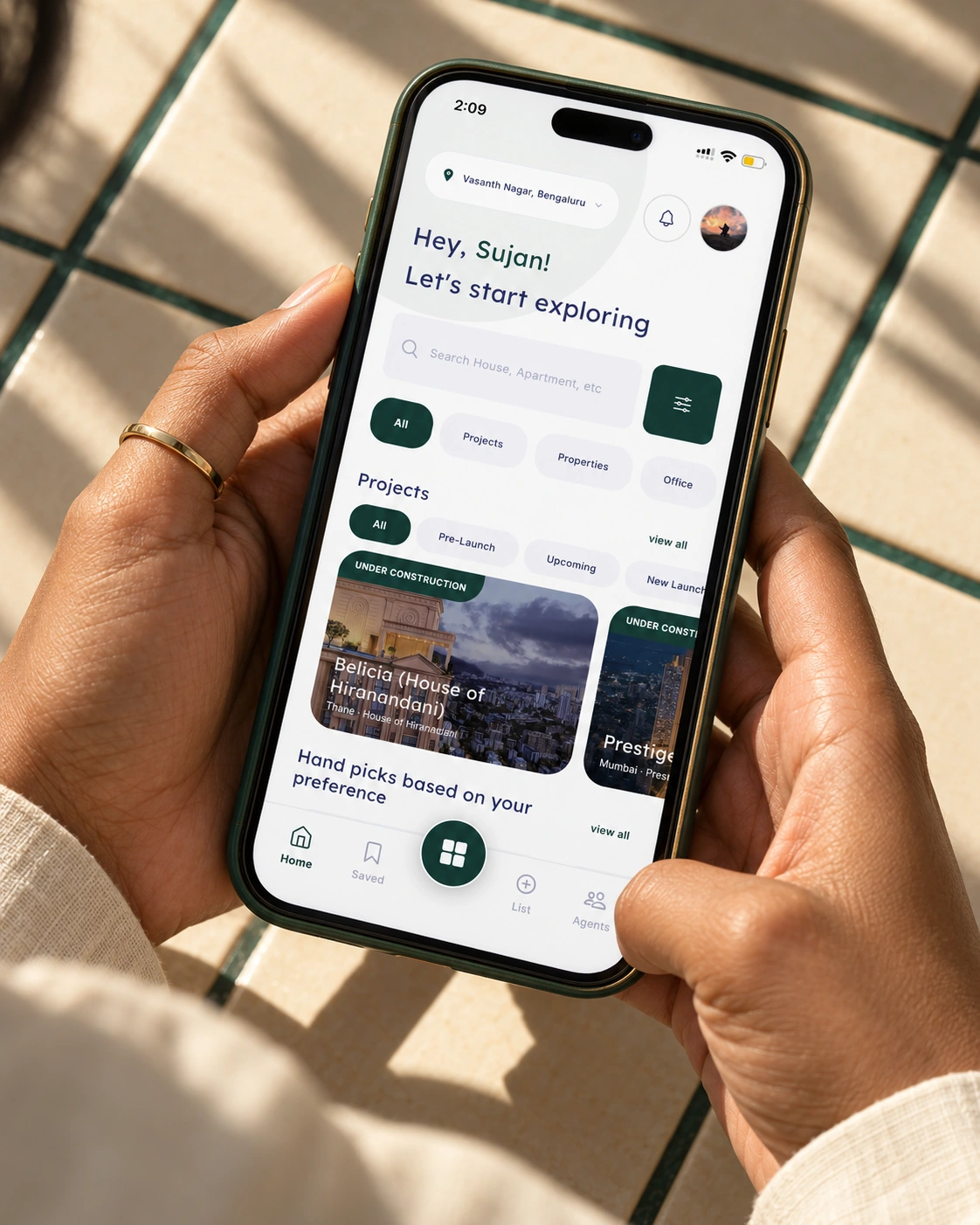A person holding the 27 Estates property discovery app in an emerald and gold phone case in natural sunlight